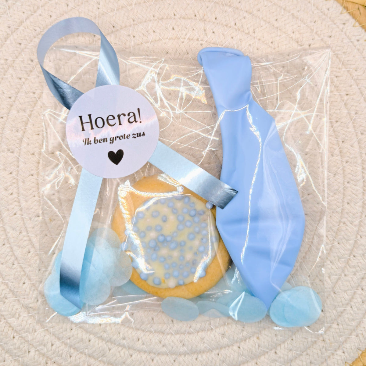 Kant-en-klare geboortetraktatie van Mila Trakteert met een blauw geboortekoekje in een cellofaanzakje met blauwe confetti, een blauwe ballon en een sluitsticker met de tekst Een broertje.