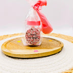 Geboorte traktatie meisje: roze babyflesje gevuld met roze en witte spekjes in cellofaan met lint, speentje en roze sticker.