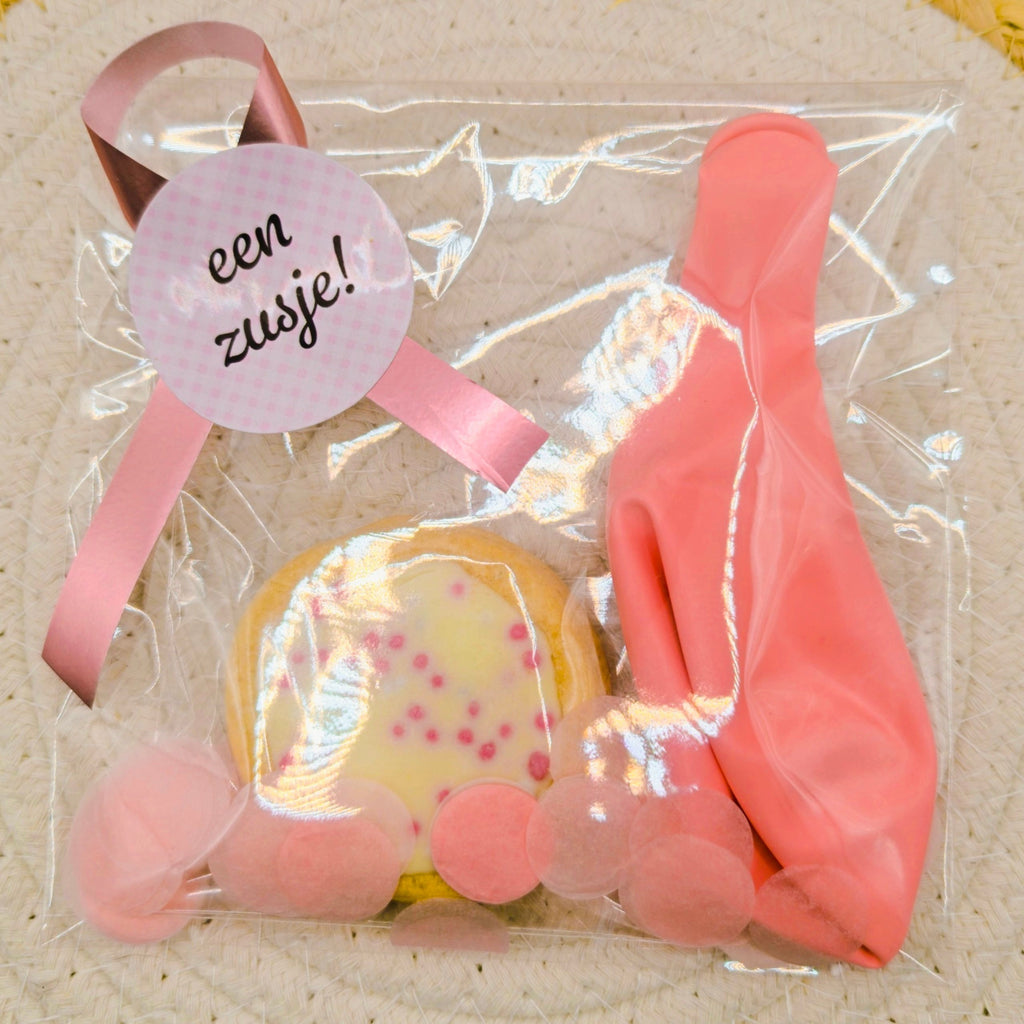 Roze geboorte traktatie van Mila Strakteert in transparante verpakking met een roze ballon, een zakje confetti, een geboortekoekje met roze muisjes en een roze sticker.