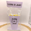 Een kant-en-klare popcorn traktatie in een transparant blokzakje met roze-wit ruitjespatroon, gepersonaliseerd met de tekst Djuna 10 jaar.