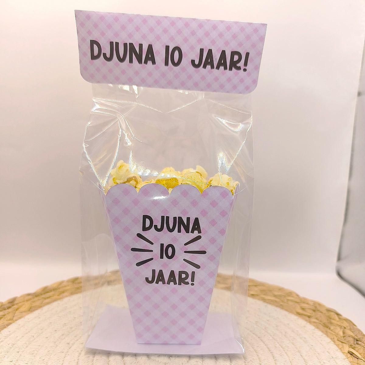 Een kant-en-klare popcorn traktatie in een transparant blokzakje met roze-wit ruitjespatroon, gepersonaliseerd met de tekst Djuna 10 jaar.